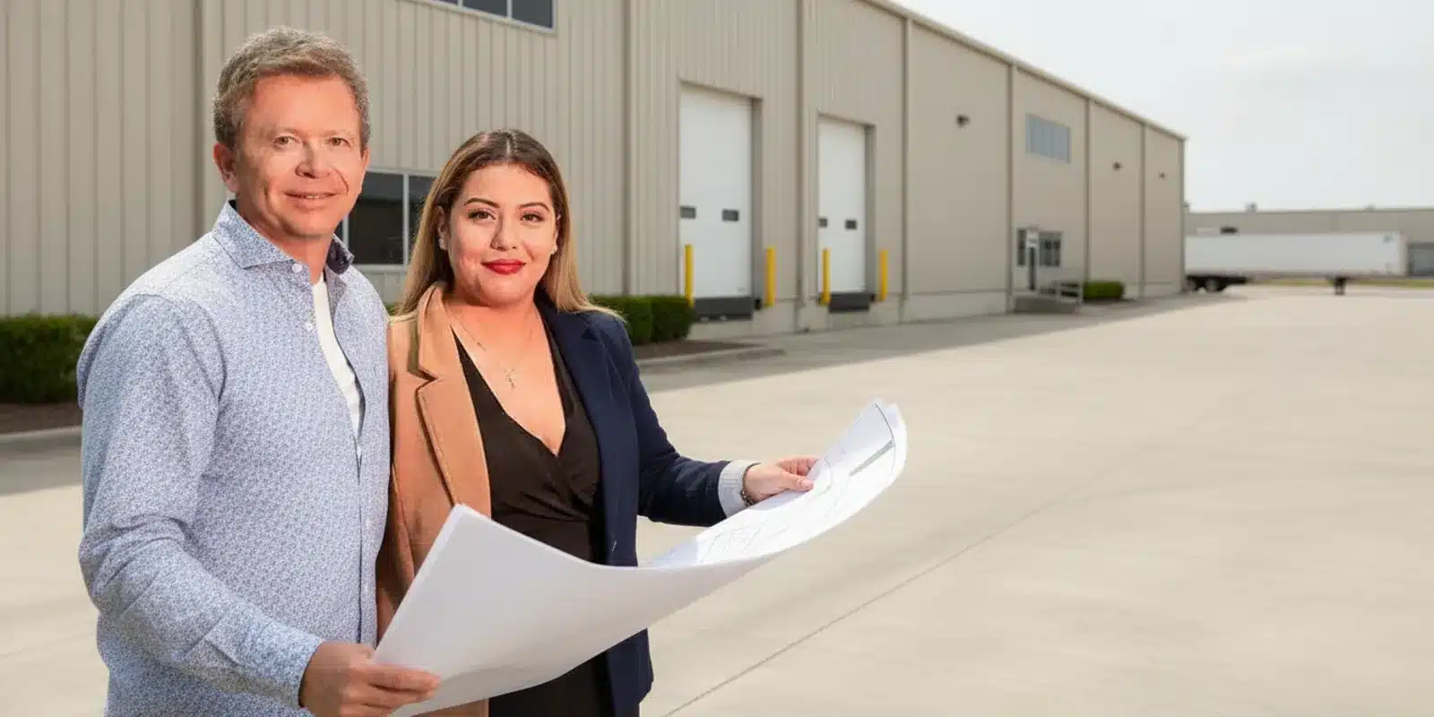 Investor and commercial property professional reviewing plans outside an industrial warehouse
